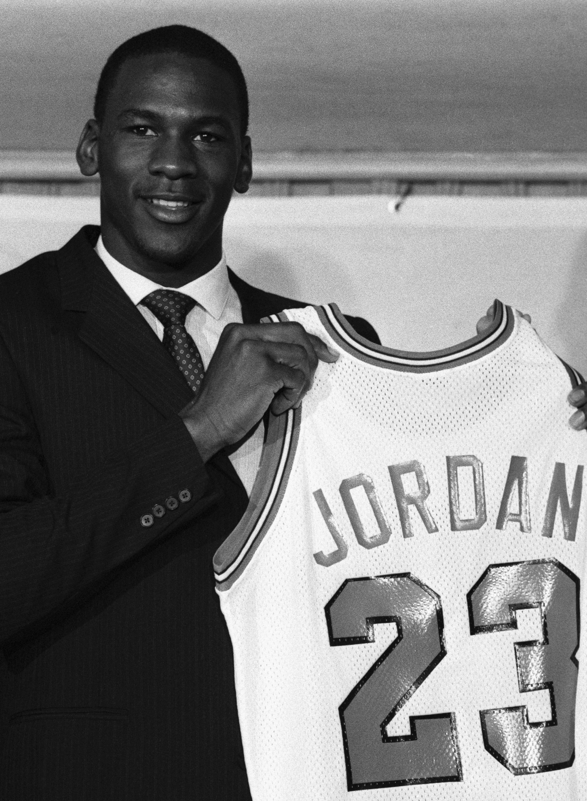 A general manager speaking at a press conference, with team logo visible in the background, discussing roster decisions.