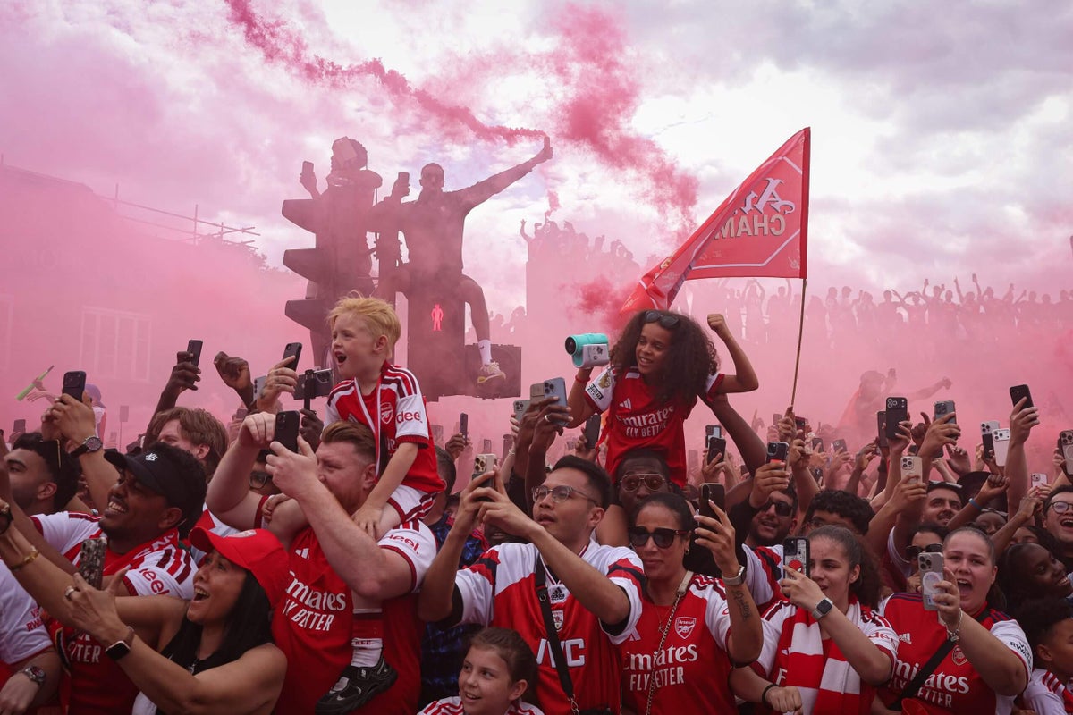Arsenal players on their team bus celebrating their Premier League title win with fans lining the streets.