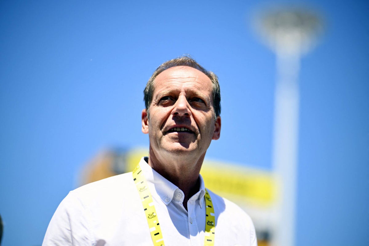 Tour de France General Director Christian Prudhomme engages in conversations with local officials while standing by a road in the French countryside.