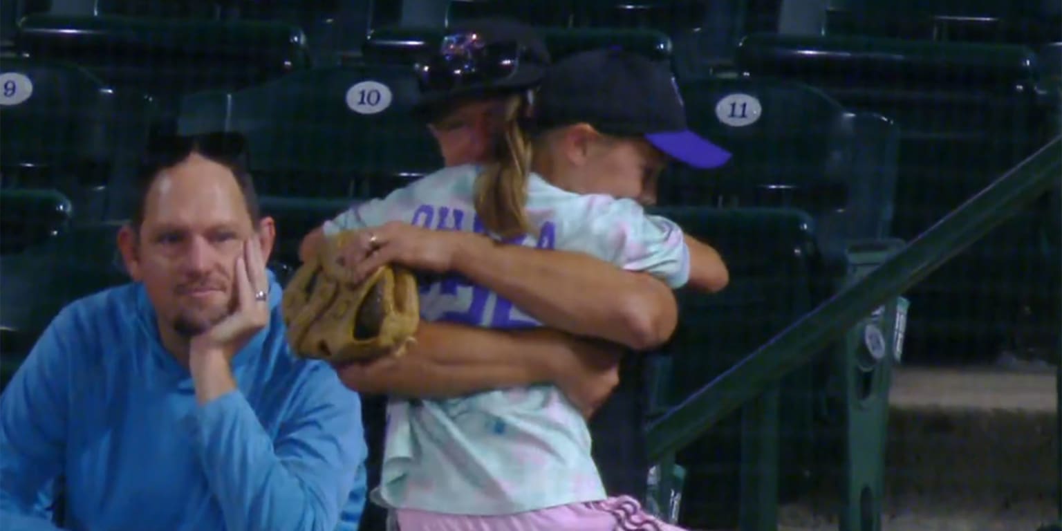 A young baseball fan beams with happiness after catching a foul ball, celebrating the moment in the stands at Coors Field.