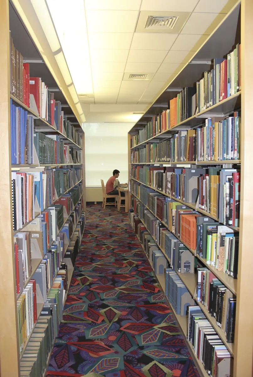 Student with a laptop and a baseball cap on a table in a library, studying between sports games